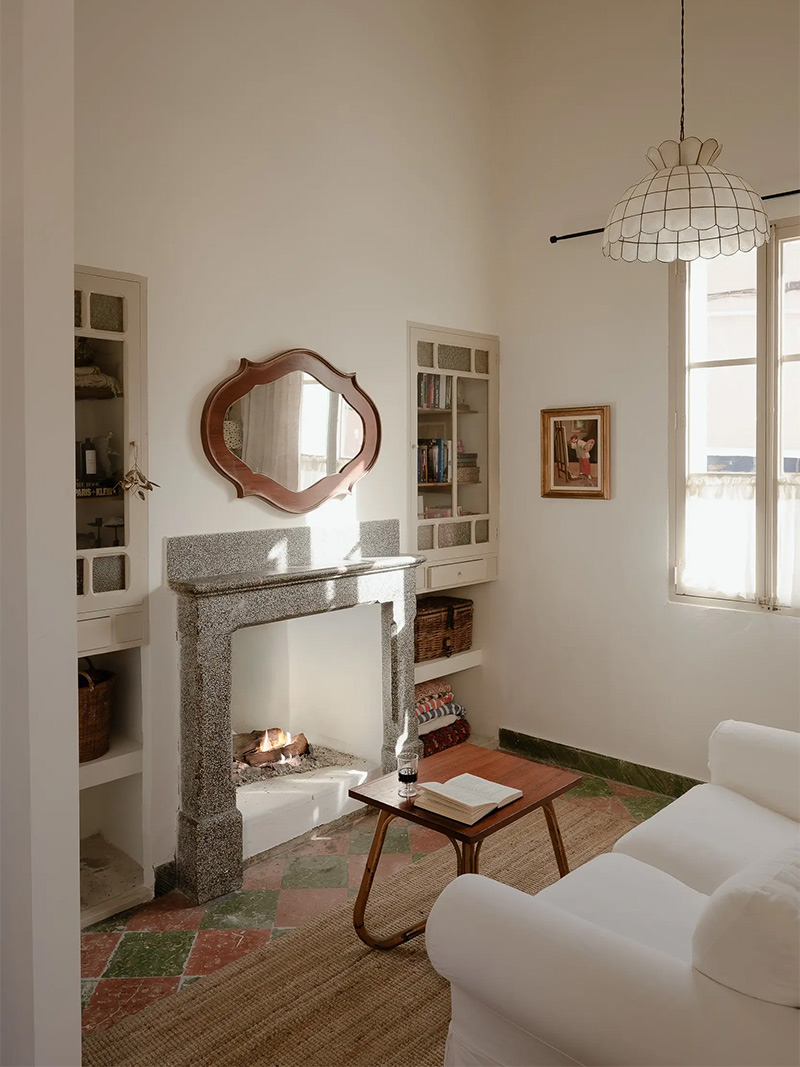 Le salon à la décoration minimalisme chaleureuse avec sa vieille cheminée en pierre préservée et ses bibliothèques d'origine de chaque côté, simplement repeintes