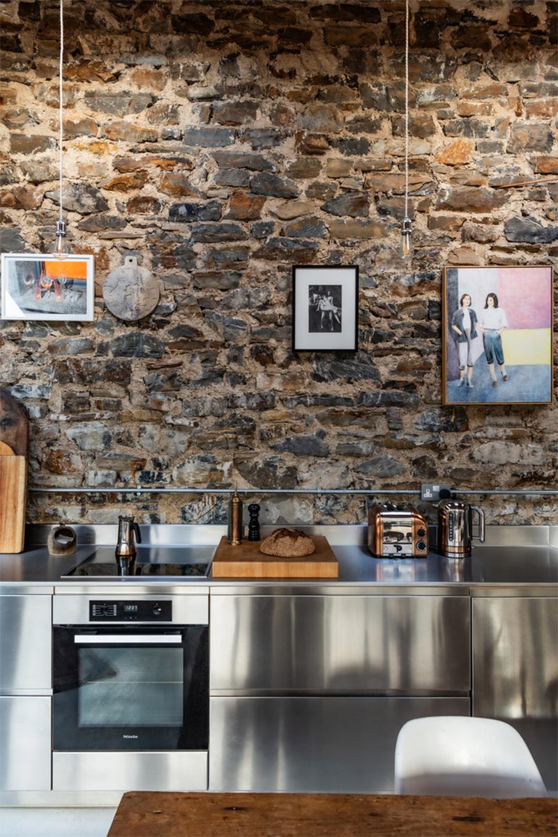 La cuisine block en inox brillant, en contraste avec le mur en pierre apparente La cuisine block en inox brillant, en contraste avec le mur en pierre apparente