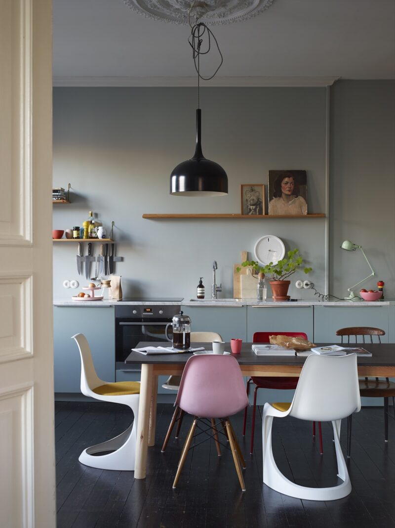 Façades de cuisine bleues avec murs assortis, plan de travail en marbre gris, sol noir radical et mobilier vintage chiné.