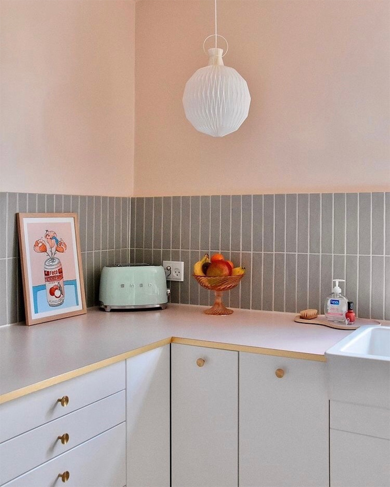 Cuisine blanche IKEA avec plan de travail rose bordé de laiton, crédence en carreaux de faïence gris et murs rose pâle.