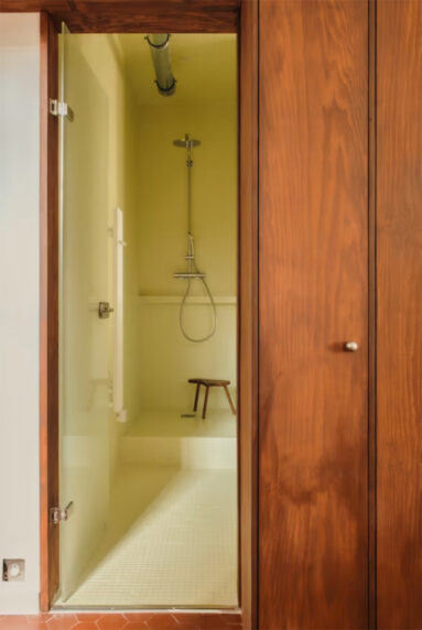 Salle de douche, pensée comme une boîte jaune, carrelée du sol au plafond avec une colonne de douche design en inox