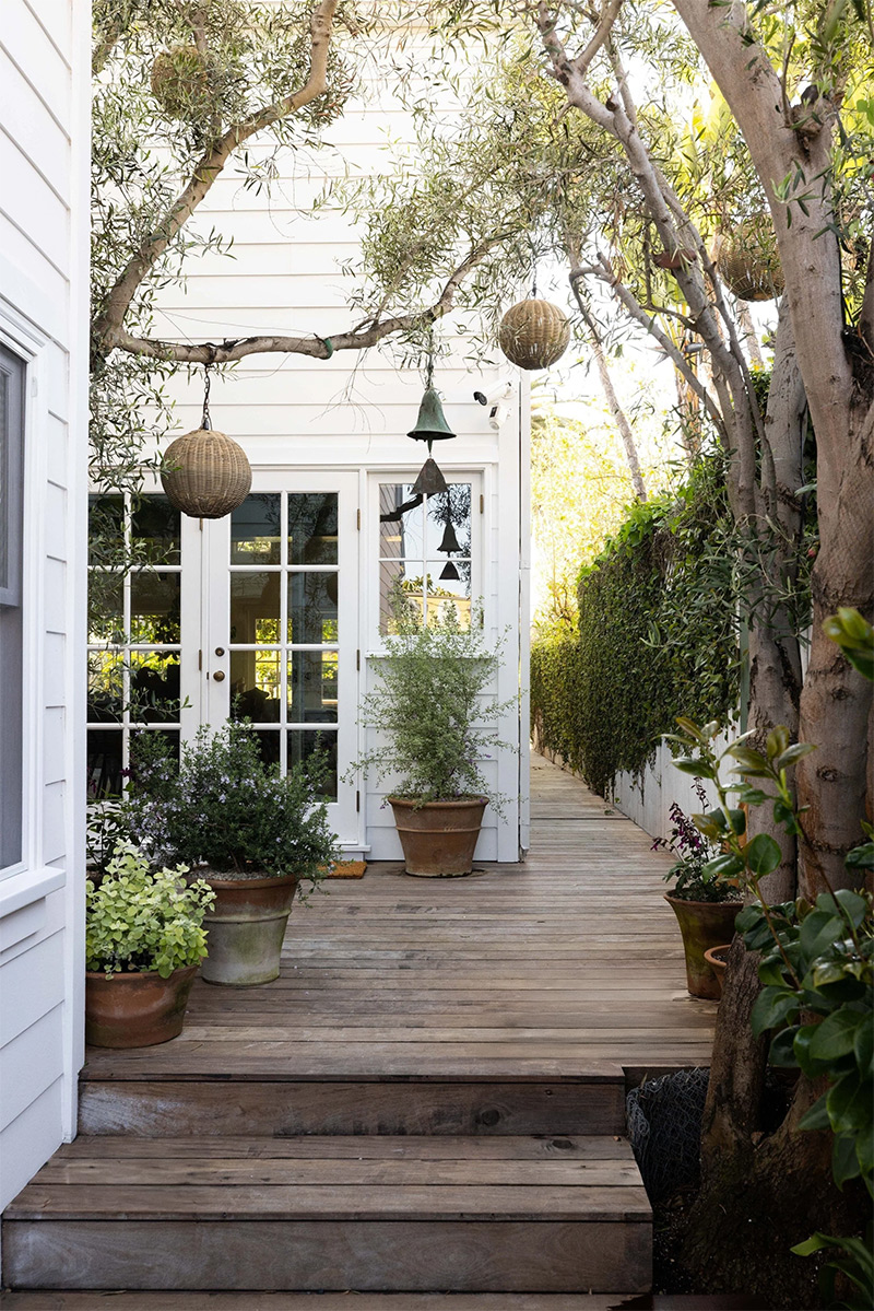 Vue extérieure de l'entrée extérieure de la maison et de son jardin, avec une terrasse aménagée en bois