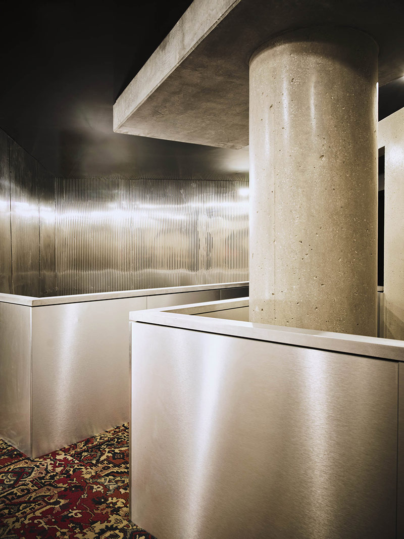 Espace desservant le restaurant en béton et inox sur lequel se reflètent les lumières