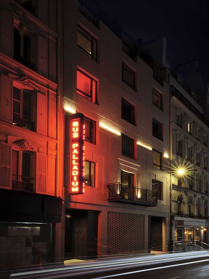 La façade du Bus Palladium à Paris, en béton sablé avec son néon rouge qui se reflète