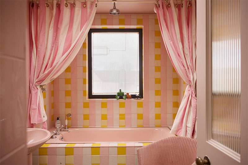 La salle de bains en damier de zelliges rose, jaune et crème et ses rideaux de douche à rayures rose et blanc