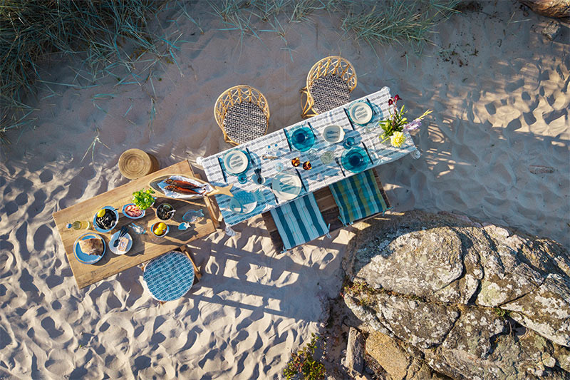 Madam Stoltz, collection été 2026 : Tables de repas, installées sur une plage de sable fin Madam Stoltz, collection été 2026 : Tables de repas, installées sur une plage de sable fin