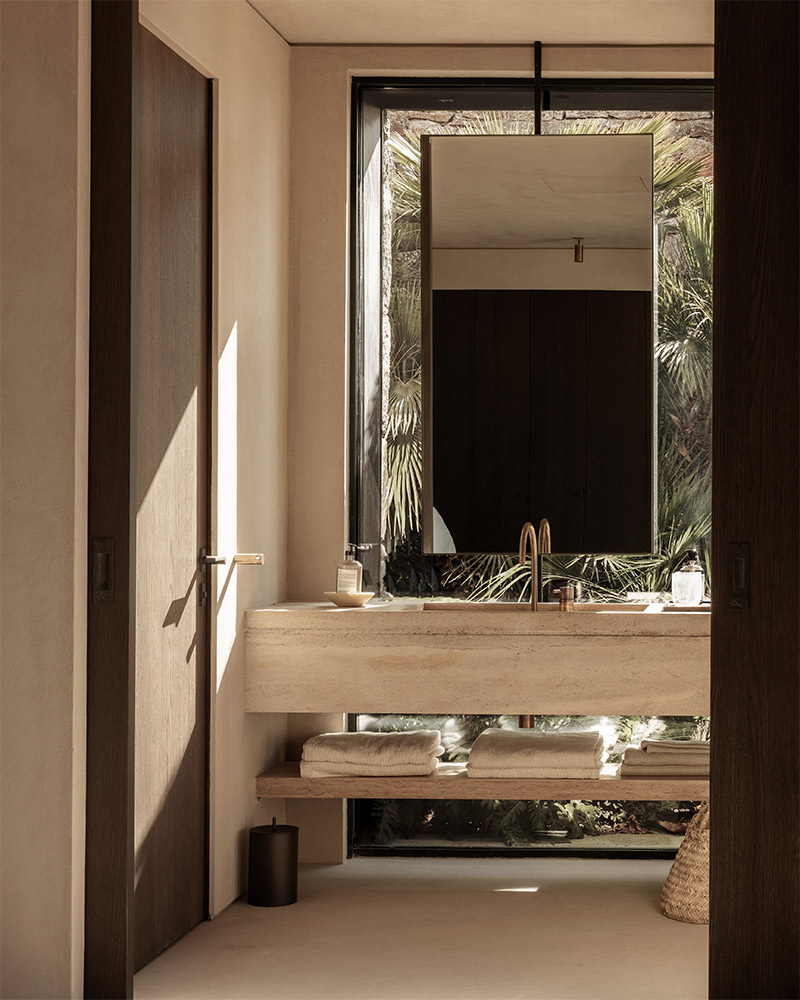 Salle de bains design ouverte sur un patio avec un lavabo en travertin et sol en béton ciré sable Salle de bains design ouverte sur un patio avec un lavabo en travertin et sol en béton ciré sable