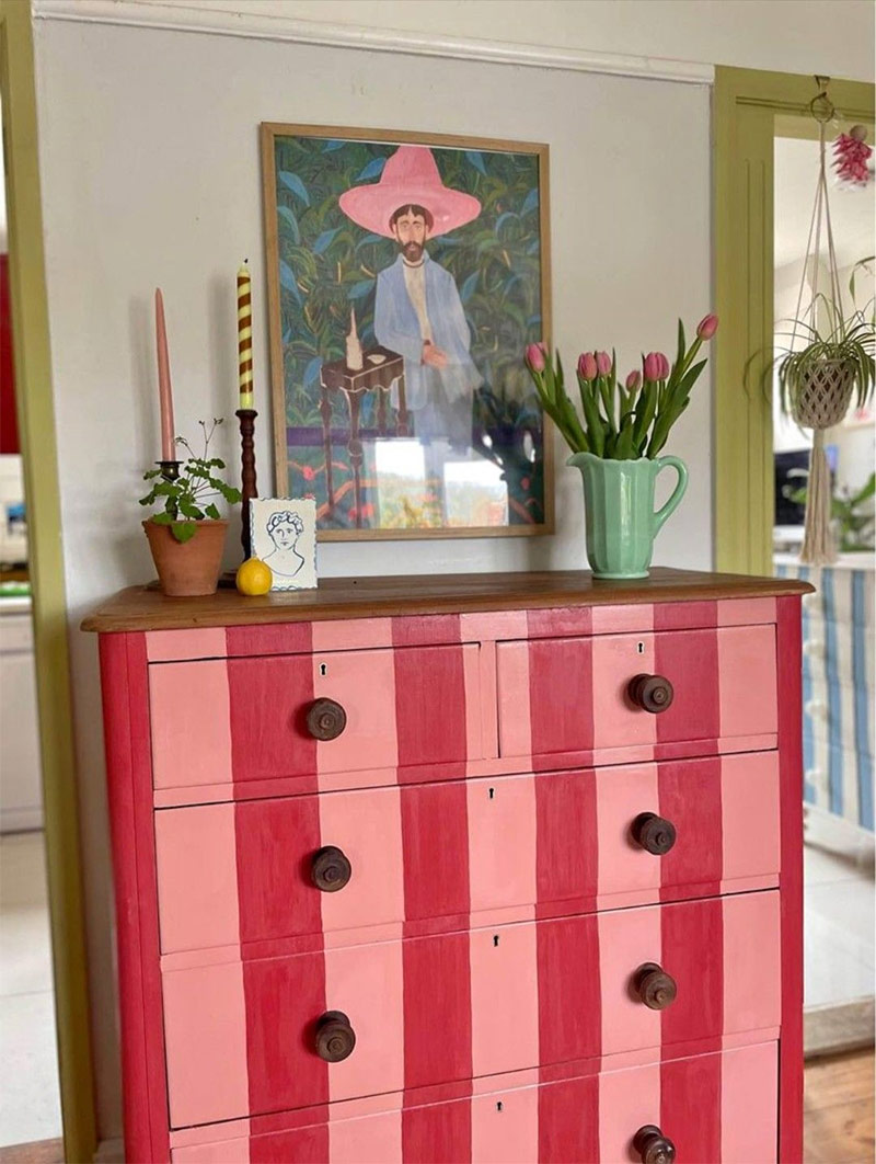 Commode ancienne au design rafraîchi avec une peinture moderne à rayures rouge et rose. Ce meuble upcyclé apporte une touche de couleur pop et de vitalité à la pièce.