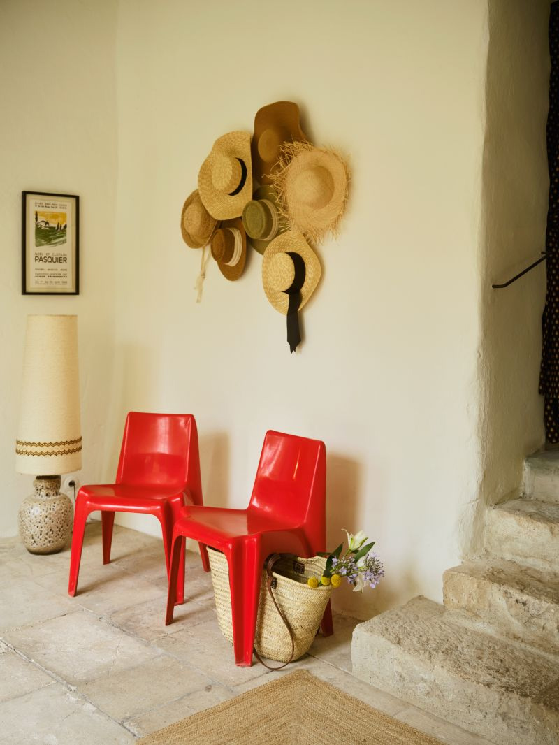 Le pied de l'escalier, avec ses deux chaises Pop en plastique rouge et sa collection de chapeaux de paille Le pied de l'escalier, avec ses deux chaises Pop en plastique rouge et sa collection de chapeaux de paille